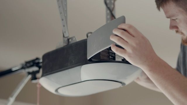A man is fixing a garage door opener in a garage.