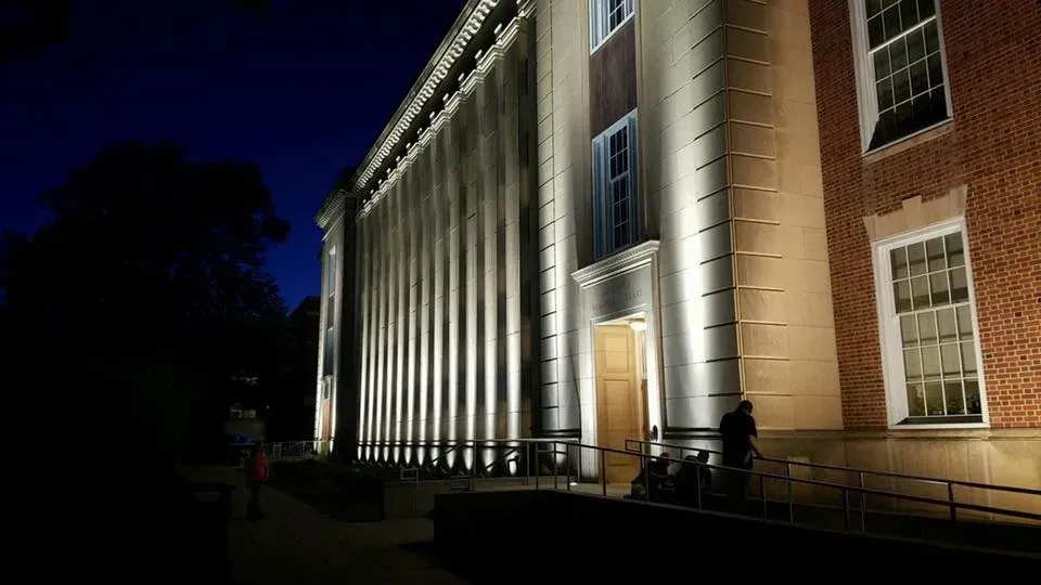 A large building is lit up at night with people walking in front of it.
