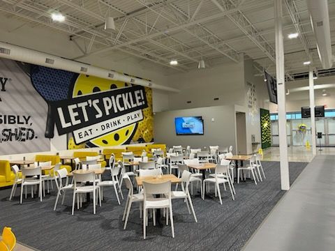 A large room with tables and chairs and a wall that says let 's pickle.
