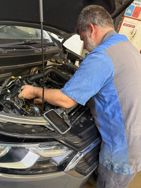 Hands holding a wrench and giving a thumbs up in front of an open car hood.
