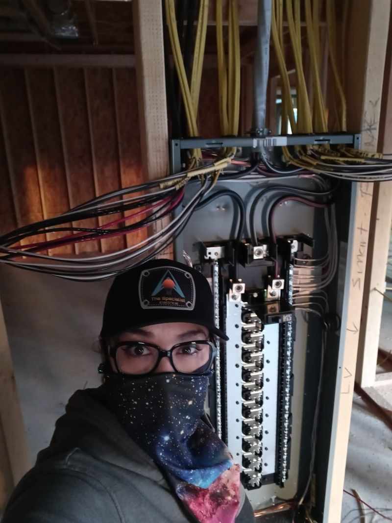 A woman wearing a mask and a hat is standing in front of an electrical box.