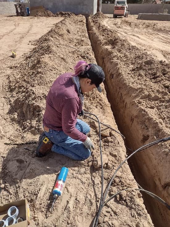 A man is kneeling in the dirt working on a pipe.