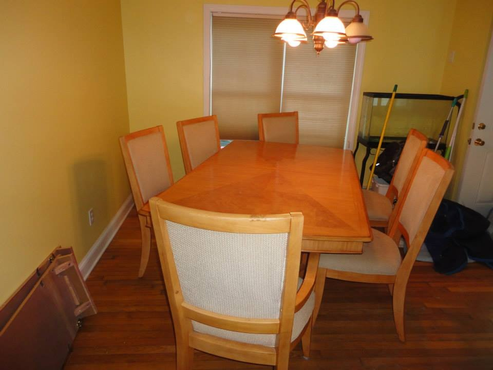A rectangular wooden dining table set with six upholstered chairs in a room with yellow walls and hardwood floors.