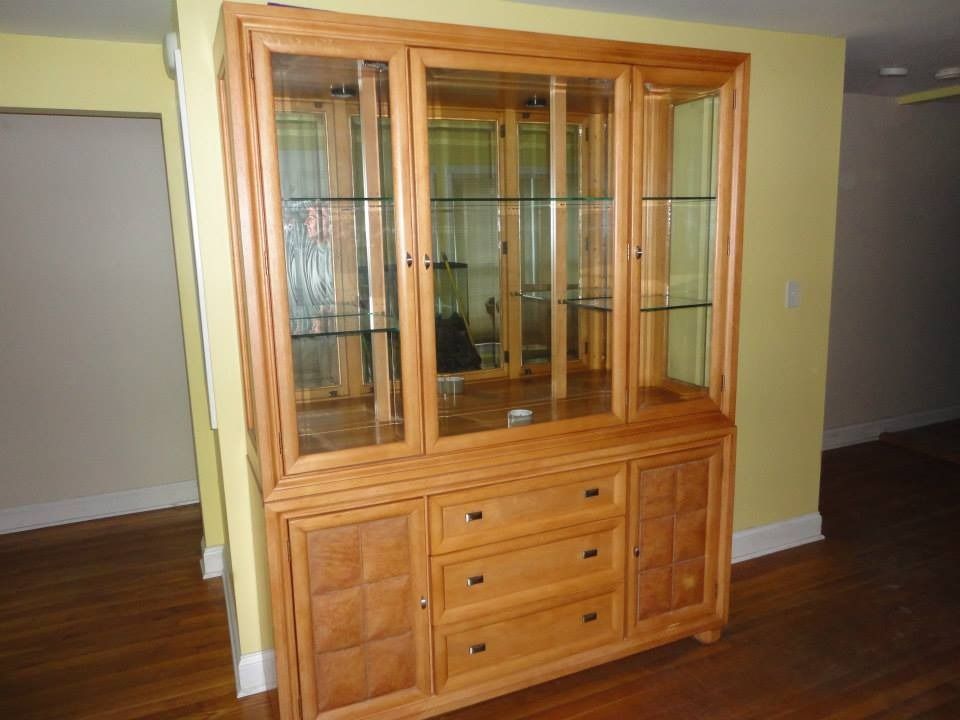 A light wood china cabinet with glass doors, shelves, three central drawers, and two textured cabinet doors.