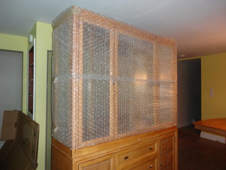 A large wooden hutch with glass-front cabinets wrapped in bubble wrap for protection in a residential room.