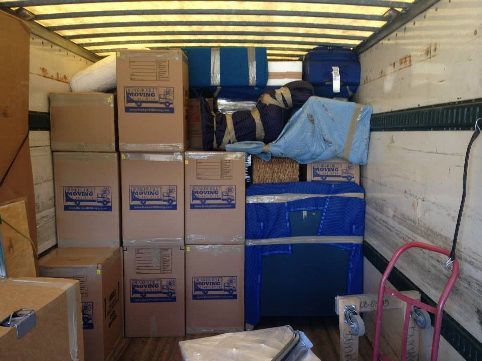 The interior of a moving truck packed with cardboard boxes and furniture wrapped in blue protective padding.