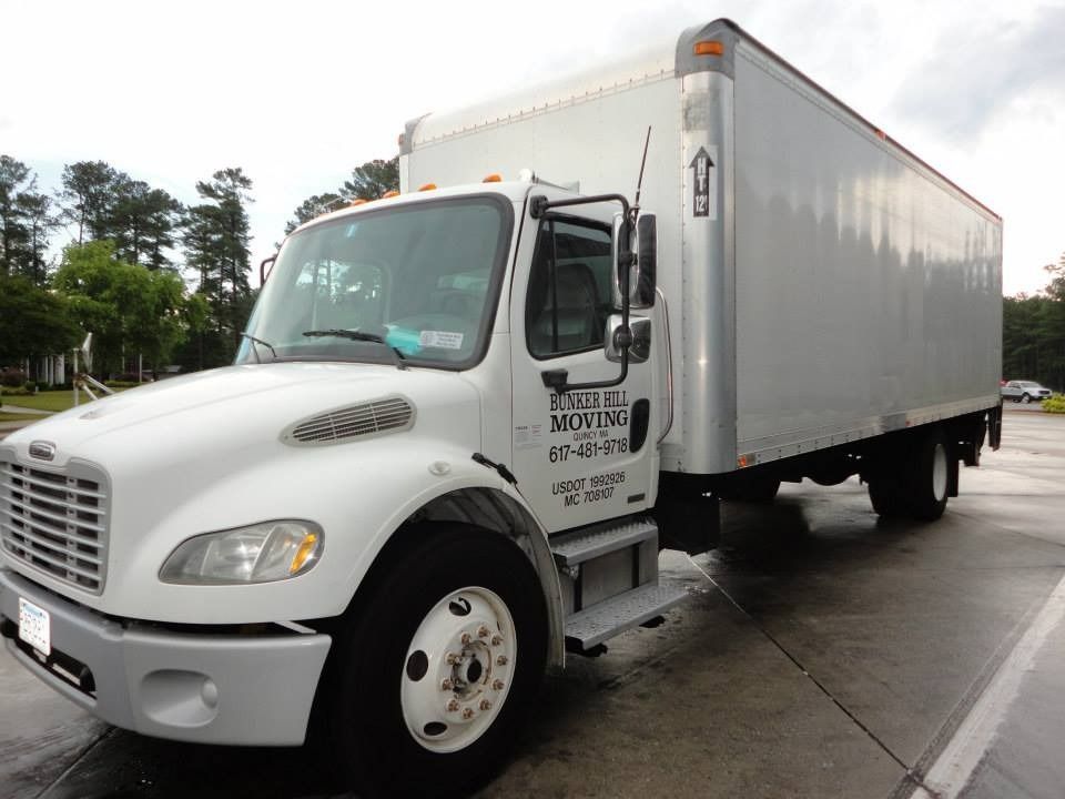A white Freightliner box truck parked in an outdoor lot on an overcast day.