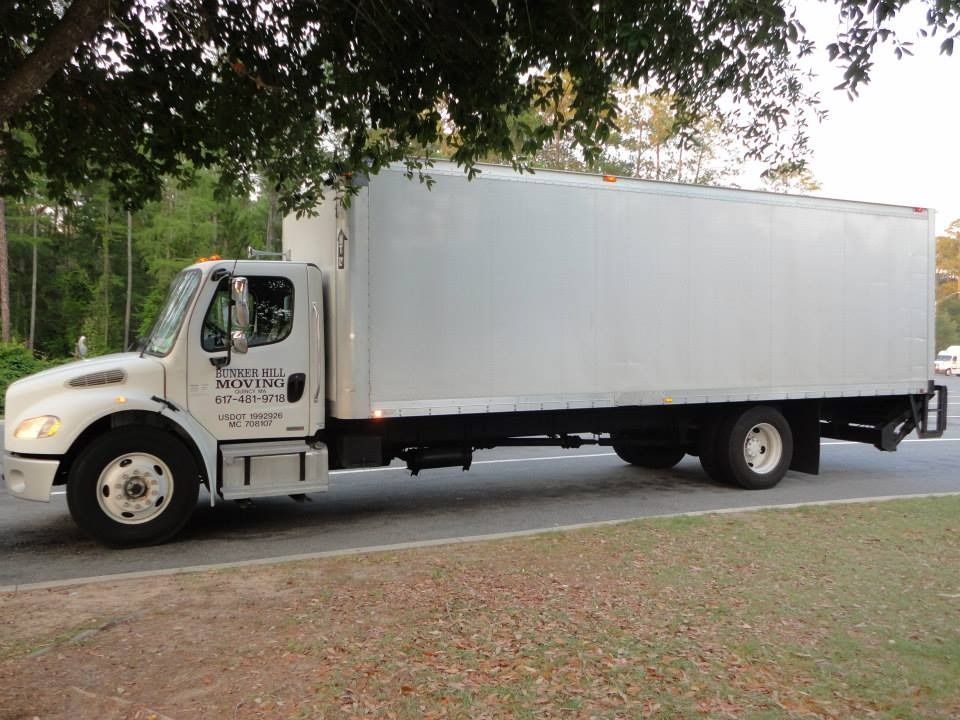 A white box truck parked on the side of a road near trees.
