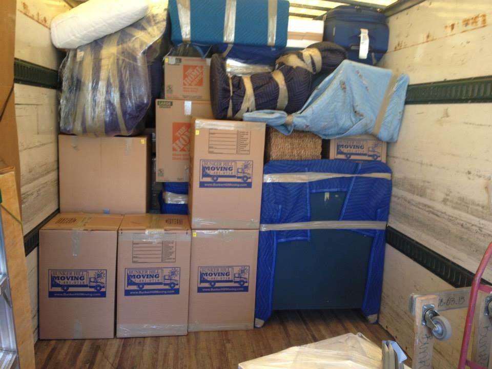 Cardboard boxes and furniture wrapped in blue plastic and moving blankets packed tightly inside a moving truck.