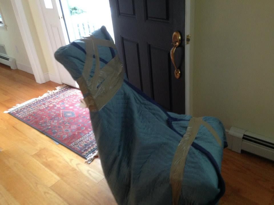 A blue furniture moving blanket wrapped around a chair and secured with beige packing tape inside a home.