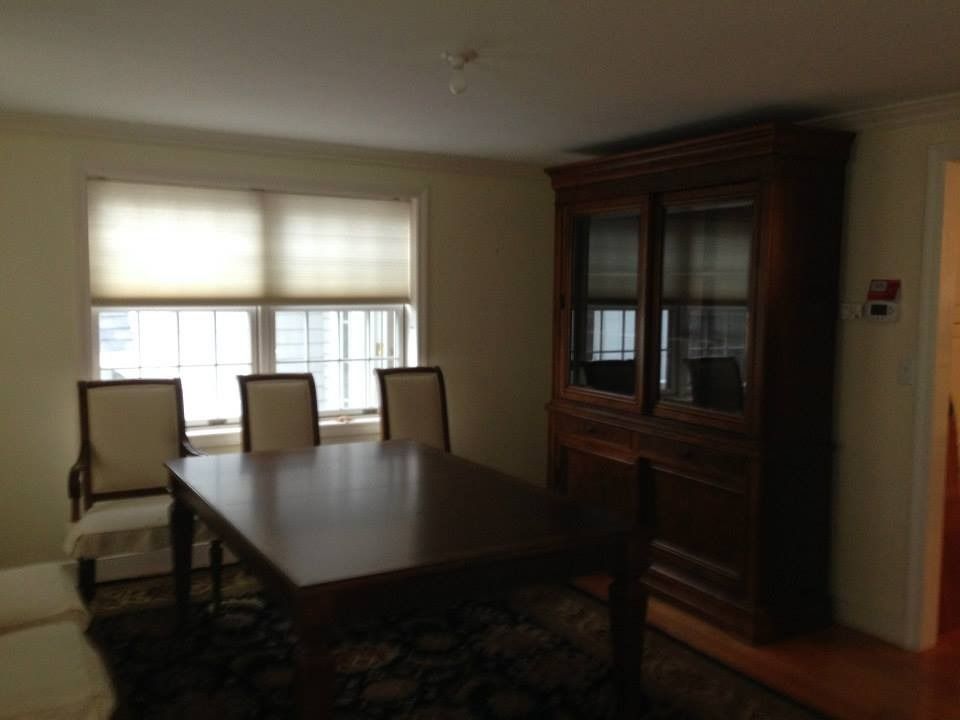 A dining room with a wooden table, three chairs, and a large dark wood hutch against a wall near a window with blinds.