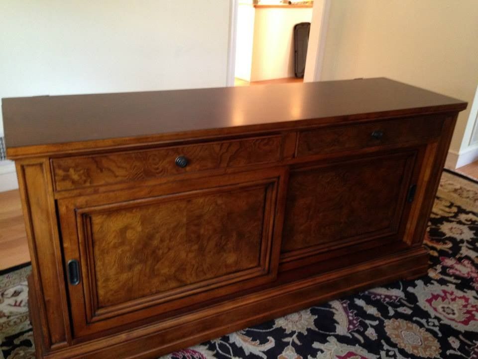 A wooden buffet cabinet with a burled wood finish, two drawers, and sliding doors, standing on a patterned rug.