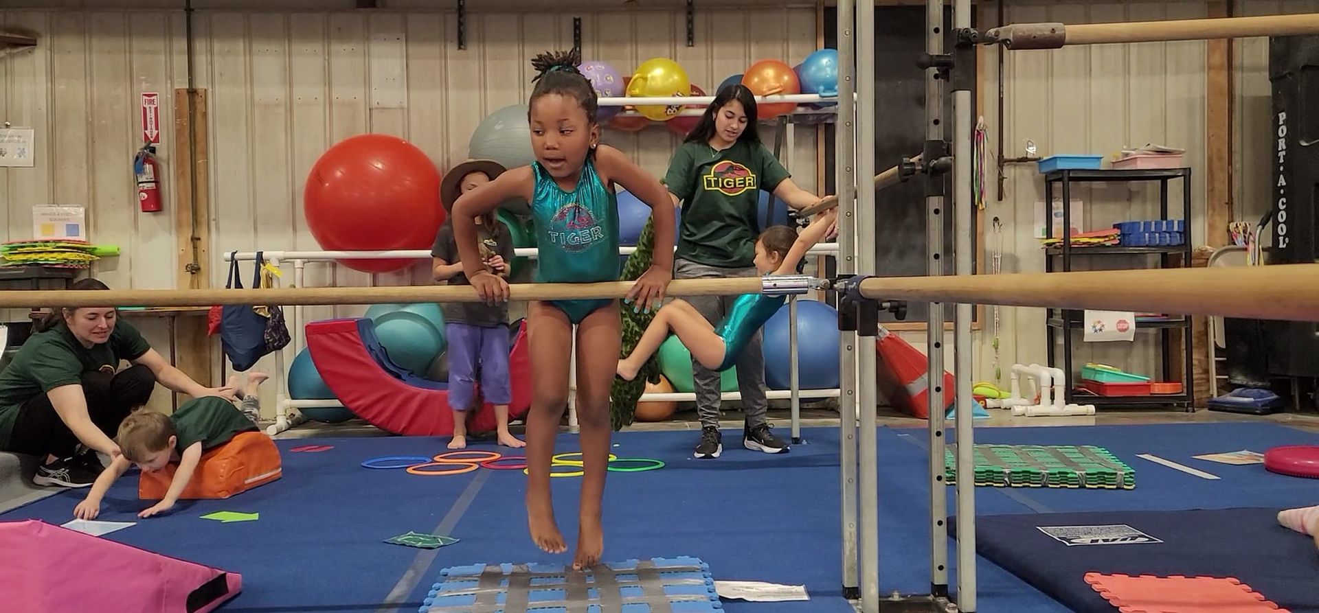 A girl is jumping over a bar in a gym.