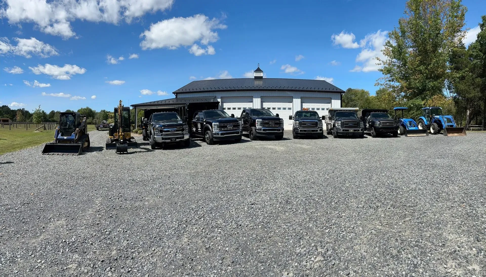 Row of parked off-road vehicles in front of a white building under a blue sky, on a gravel lot
