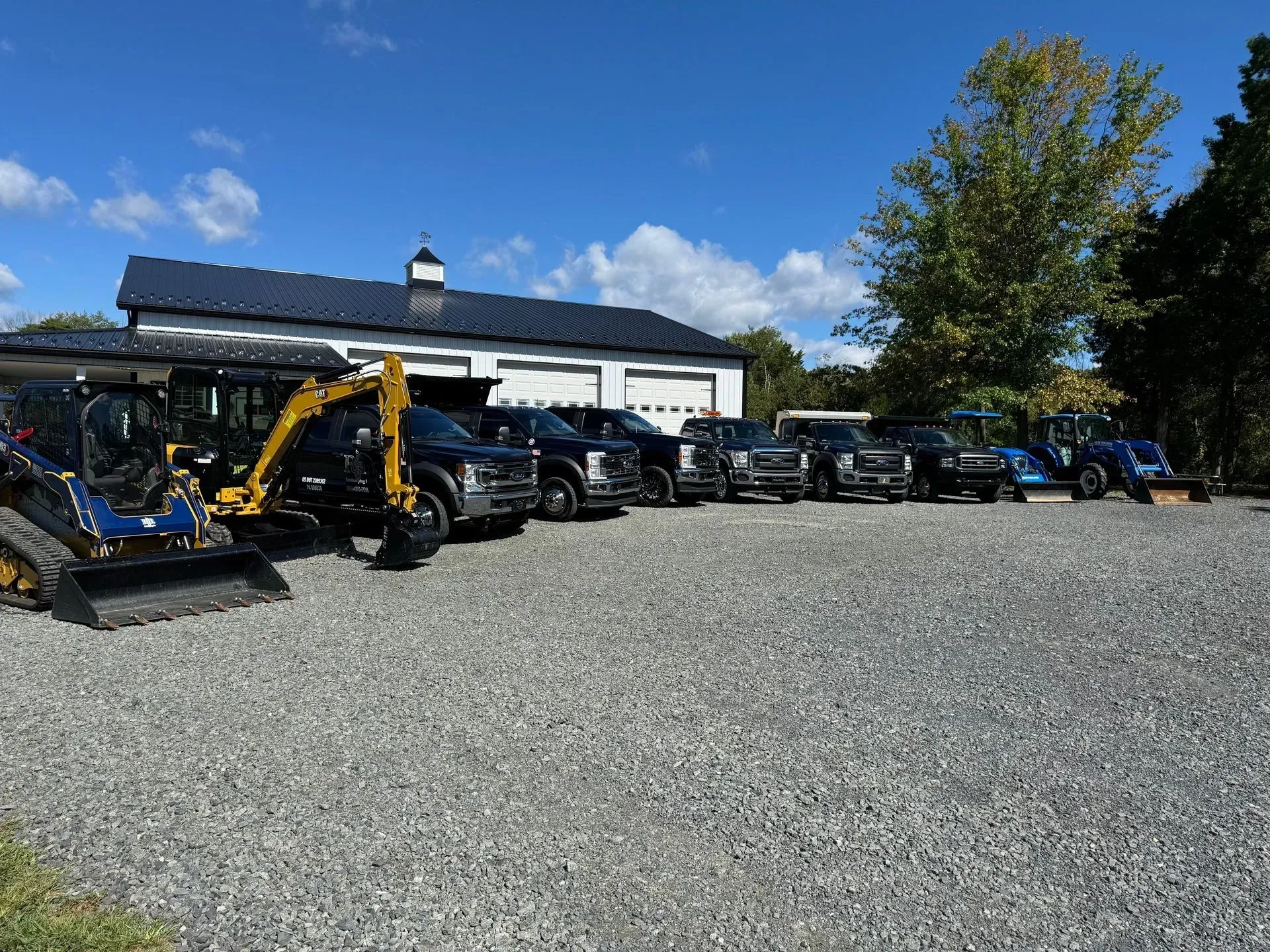 Parking lot with heavy equipment and parked vehicles beside a white building on a sunny day