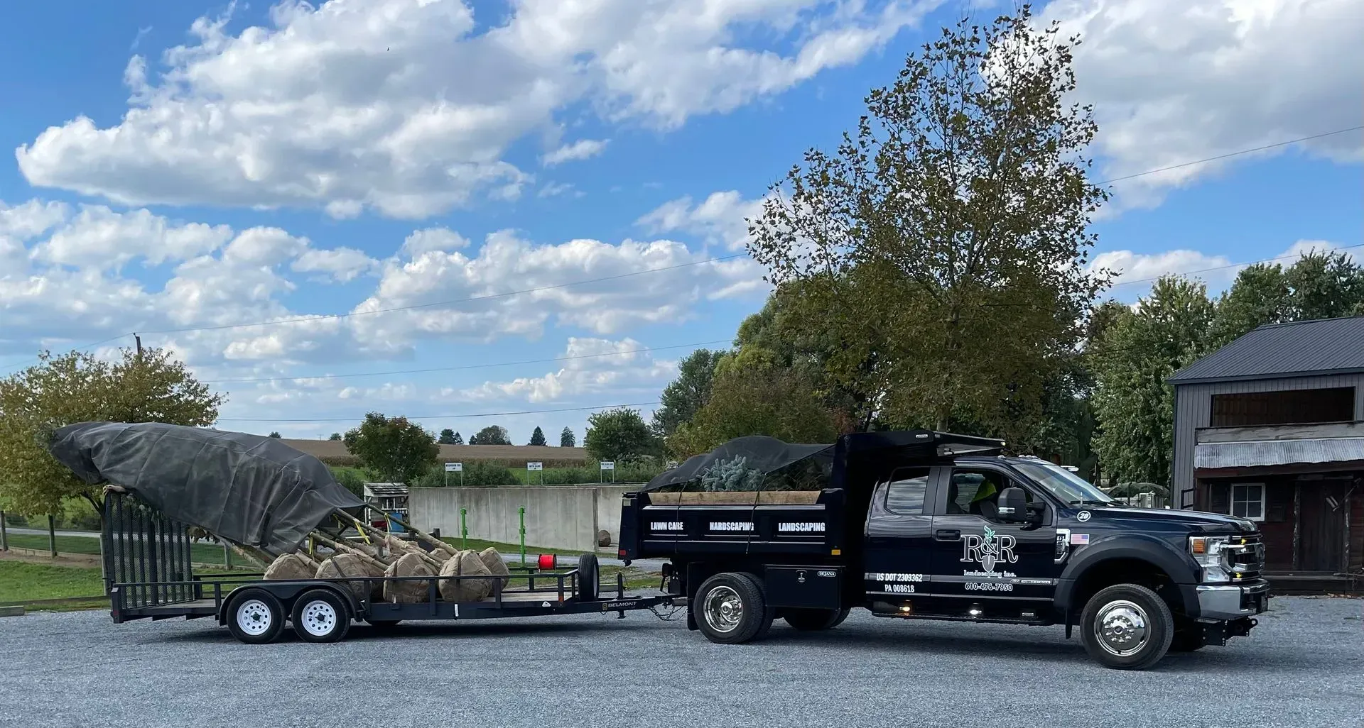 Black pickup truck towing a utility trailer with large brush piles on a gravel lot under a blue sky