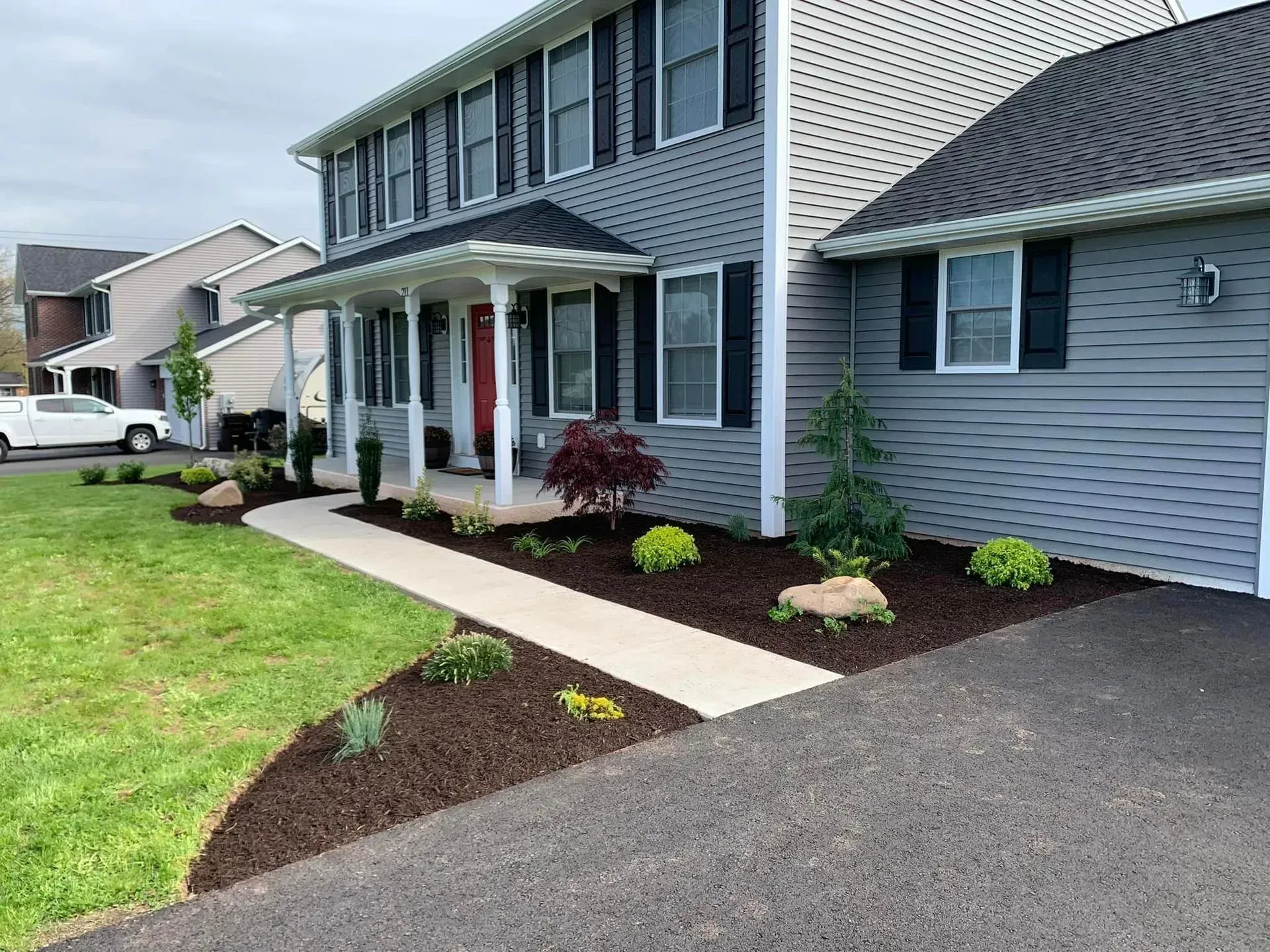 Suburban house exterior with gray siding, front porch, walkway, and landscaped flower beds