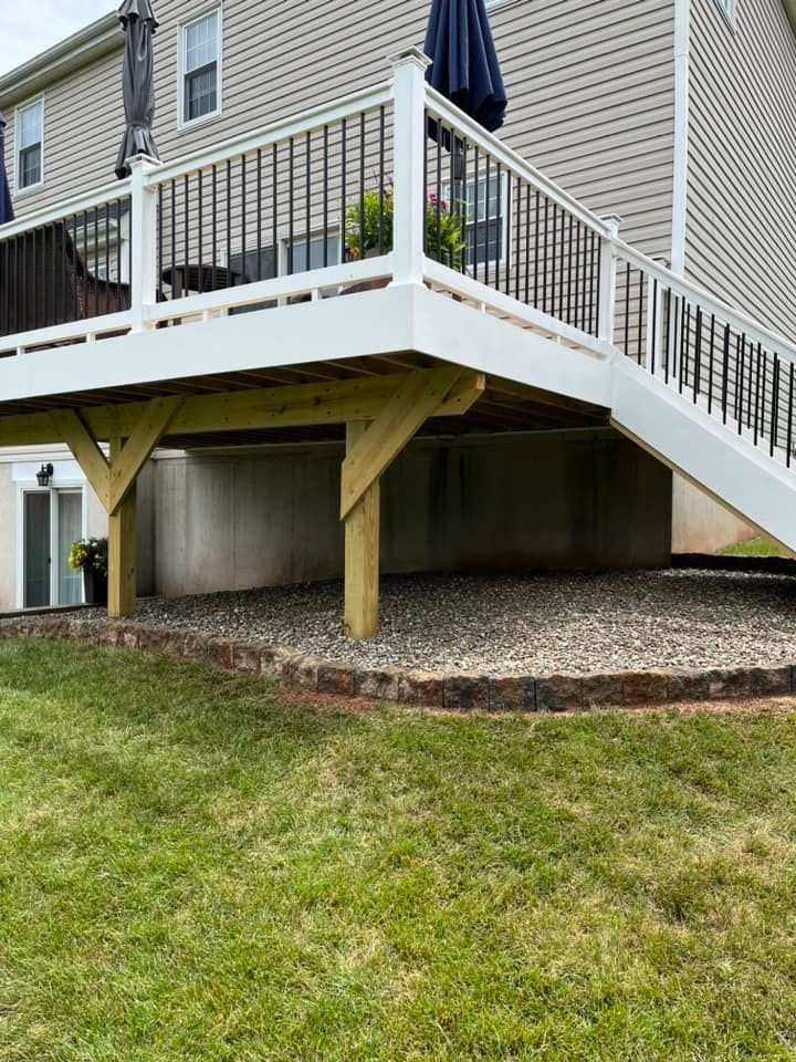 Elevated house deck with white railings and stairs over a concrete basement on a grassy yard