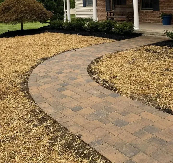 Curved brick walkway leading to a house entrance through a mulched yard