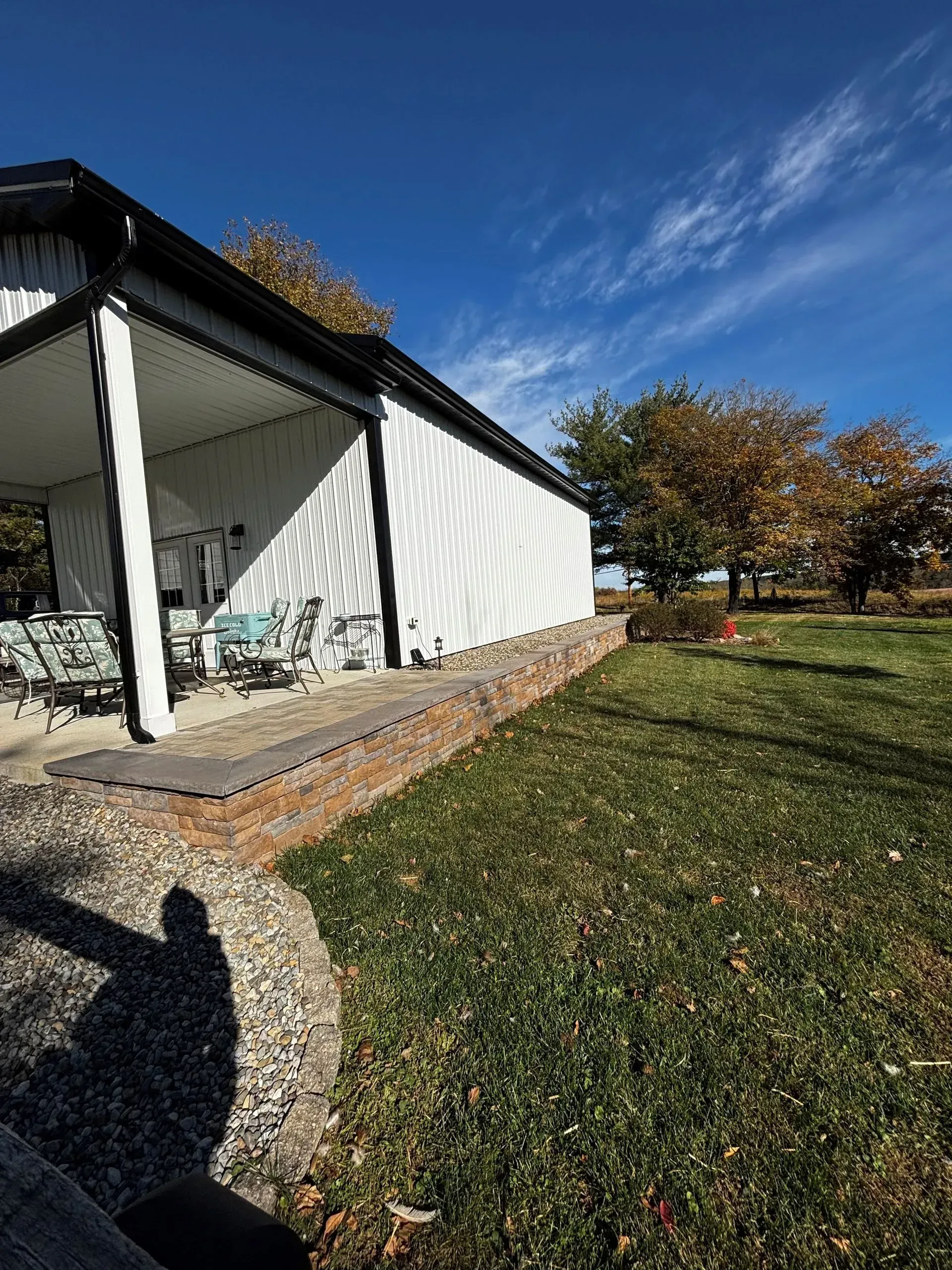 White house porch with striped awning, brick walkway, and grassy yard under a blue sky