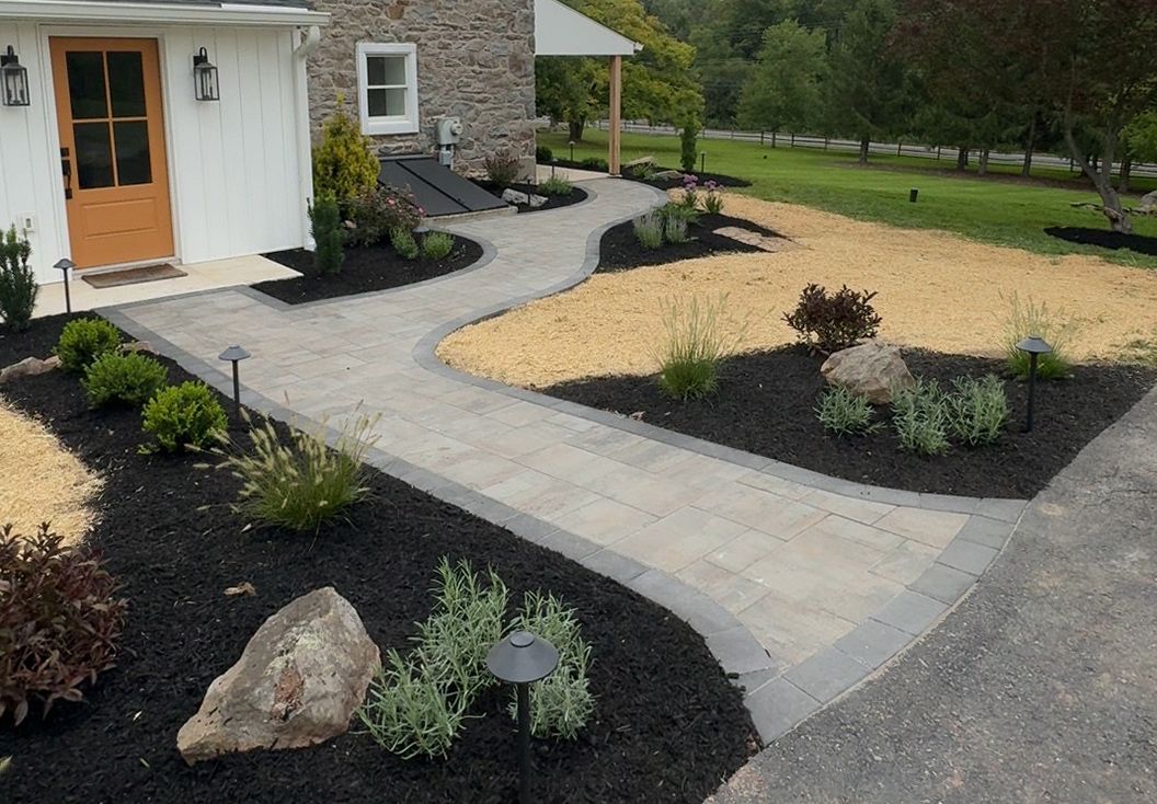 Front yard with gravel landscaping, black mulch beds, and a white house with orange front door and stone wall