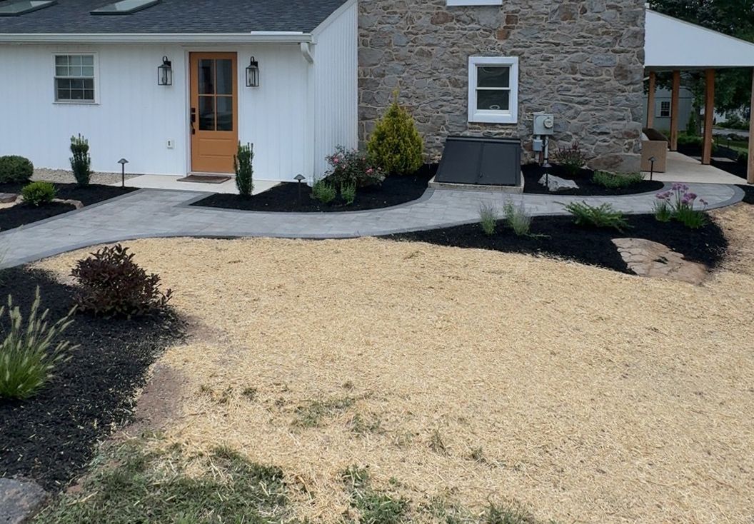 Front yard with gravel landscaping, black mulch beds, and a white house with orange front door and stone wall