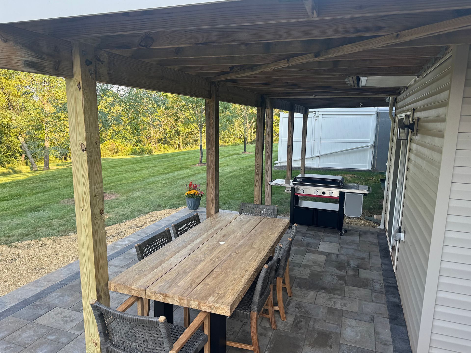 Covered patio with wooden picnic table, grill, and lake view beyond the yard