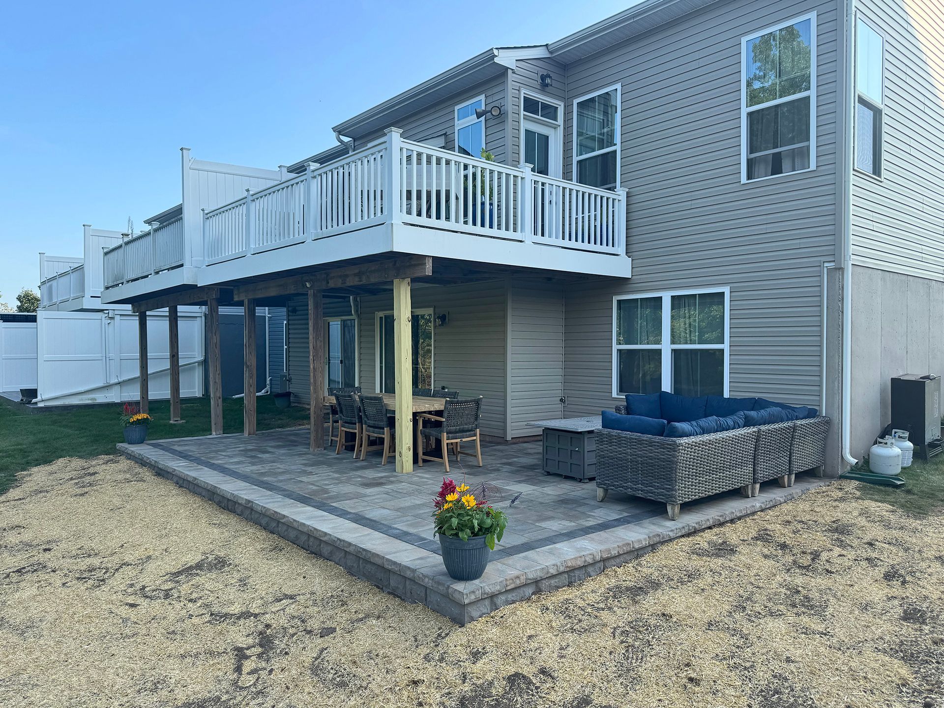 Backyard patio beside a beige house with white deck railing, stone pavers, and a large blue planter.