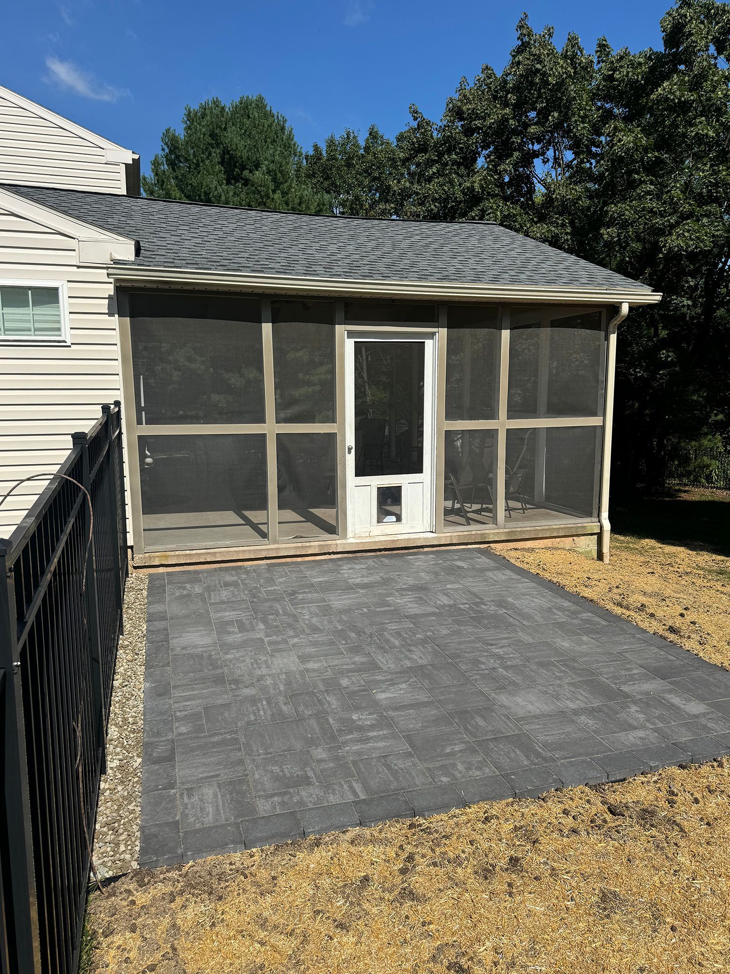 Screened porch with a white door and newly paved concrete patio beside a house