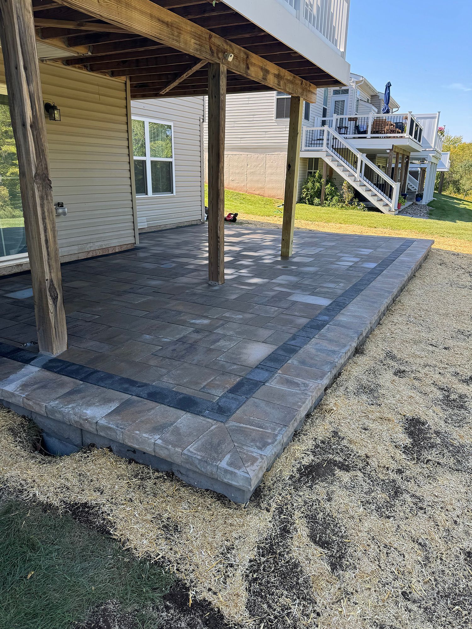 Covered concrete patio with dark stone border beside a house, over gravel ground