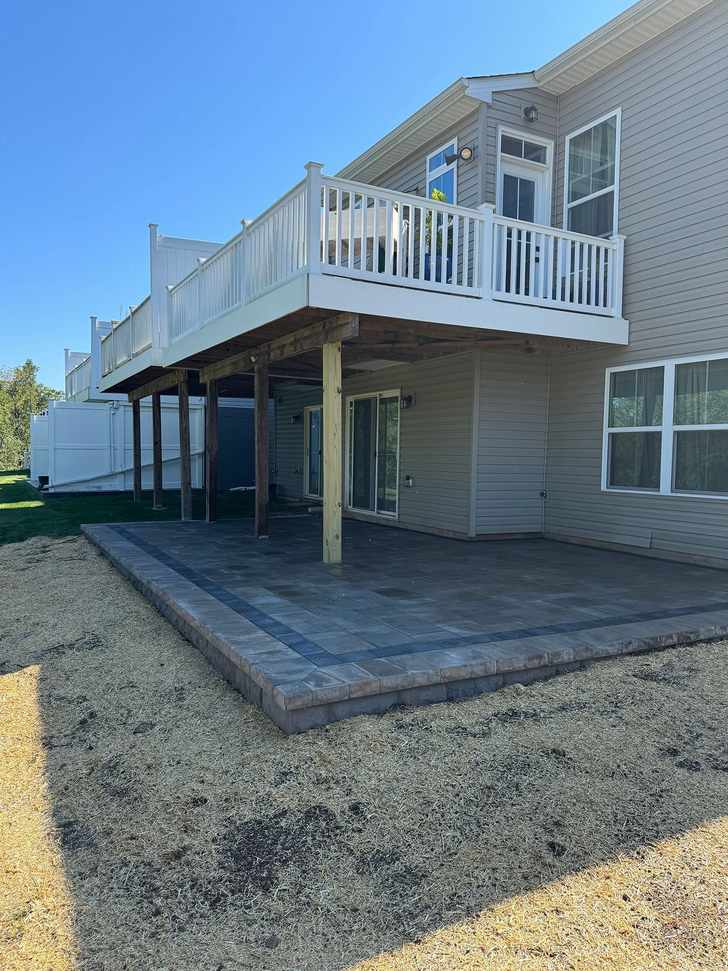 Backyard deck with white railing, concrete patio, and beige house exterior under blue sky