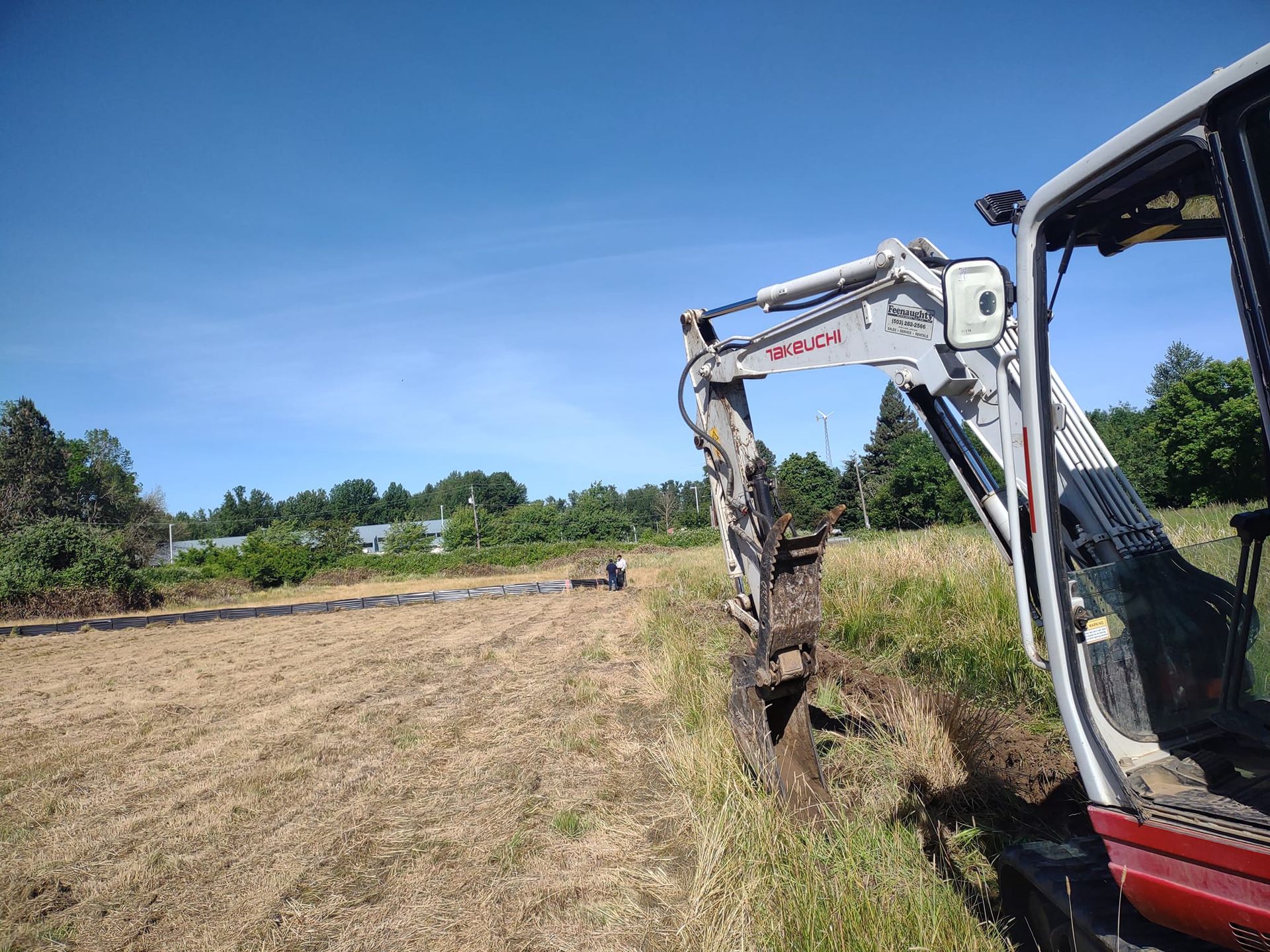 An excavator digging a trench in a field on a sunny day.