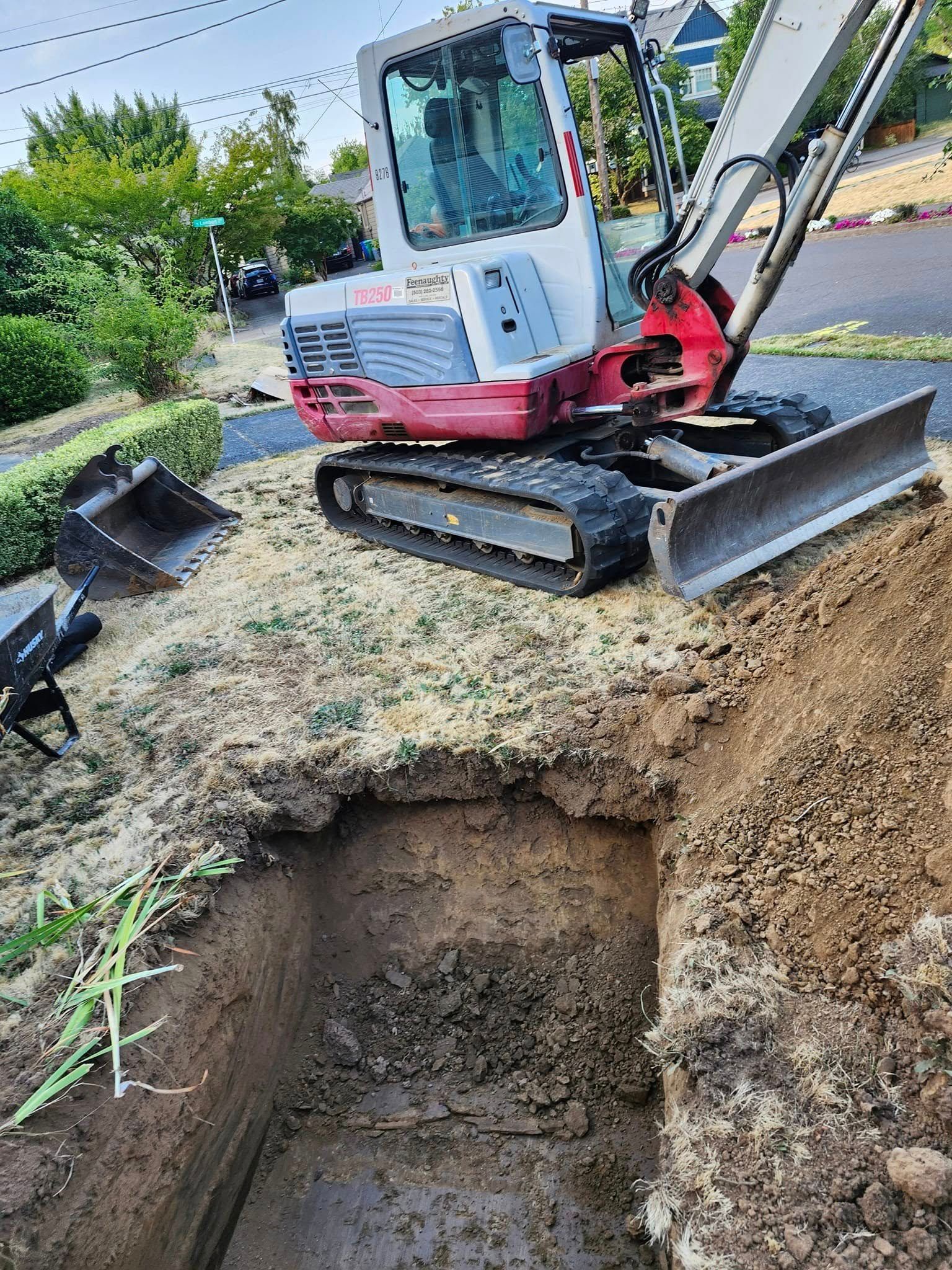 Mini excavator digging a rectangular trench in front of a house on a street.