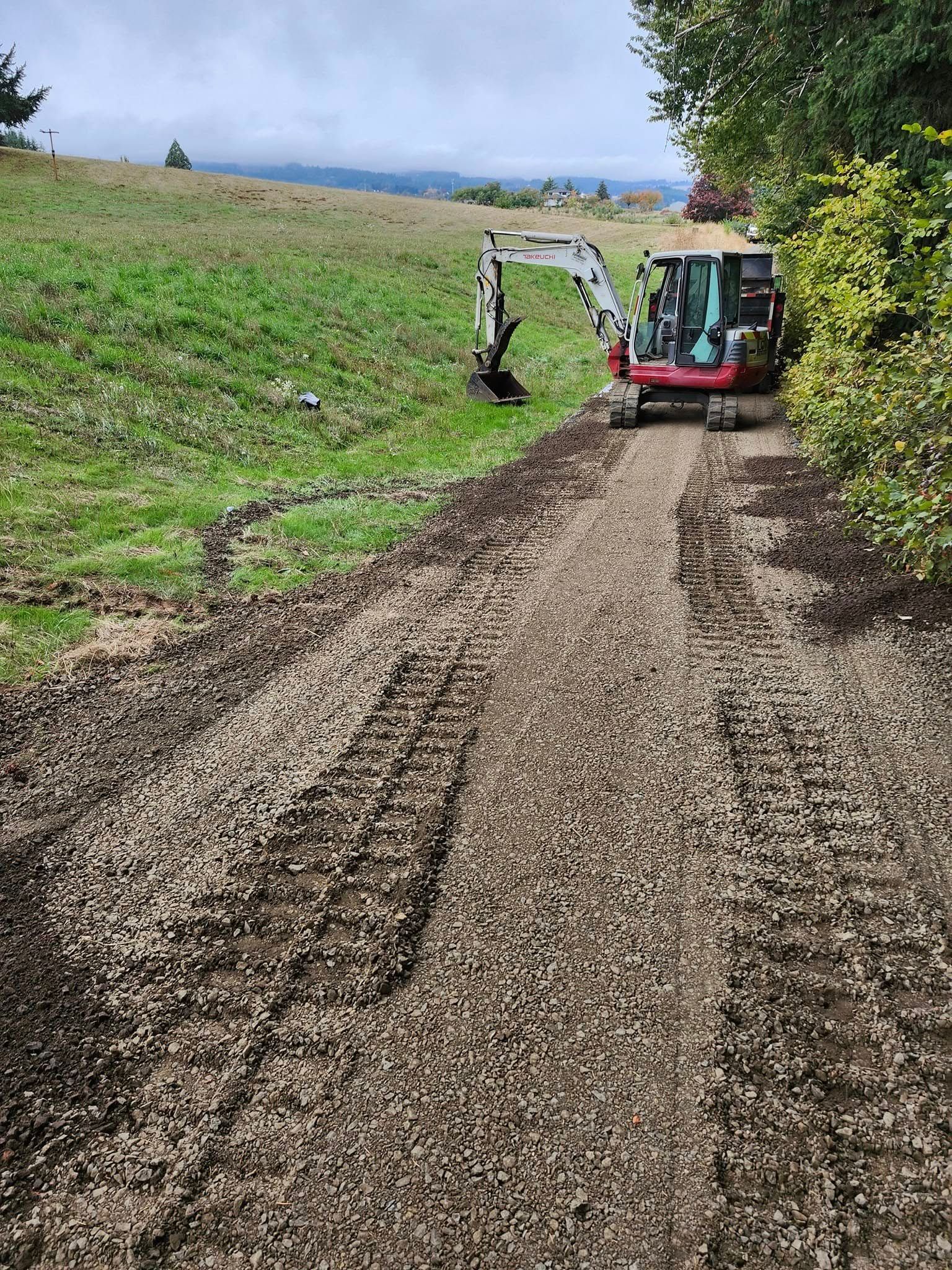 Mini excavator constructing a gravel path next to a grassy hillside.