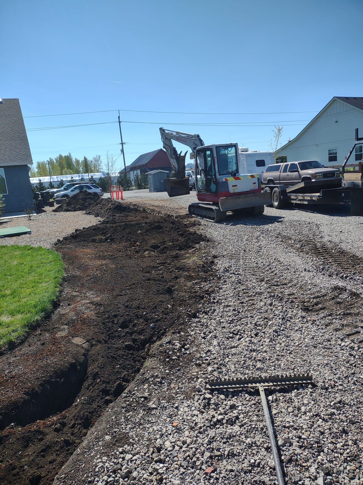 Construction site with an excavator, dark soil trench, and gravel path on a sunny day.