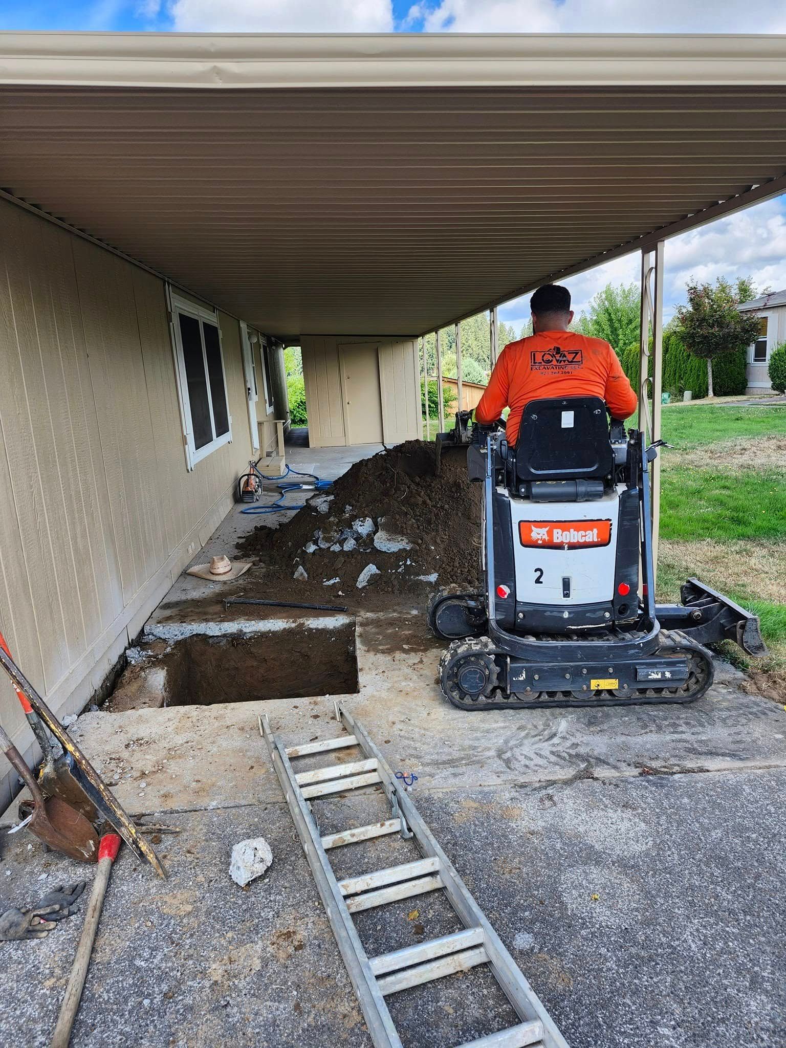 Man operating a Bobcat excavator removing debris under a covered patio.
