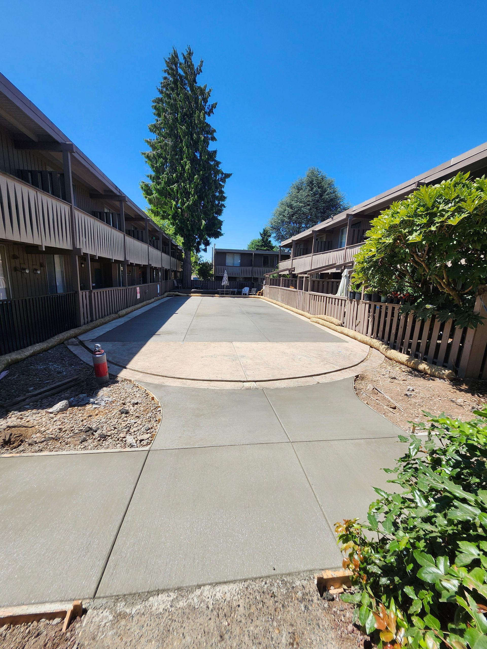 Newly poured concrete pathway between two apartment buildings under a bright blue sky.