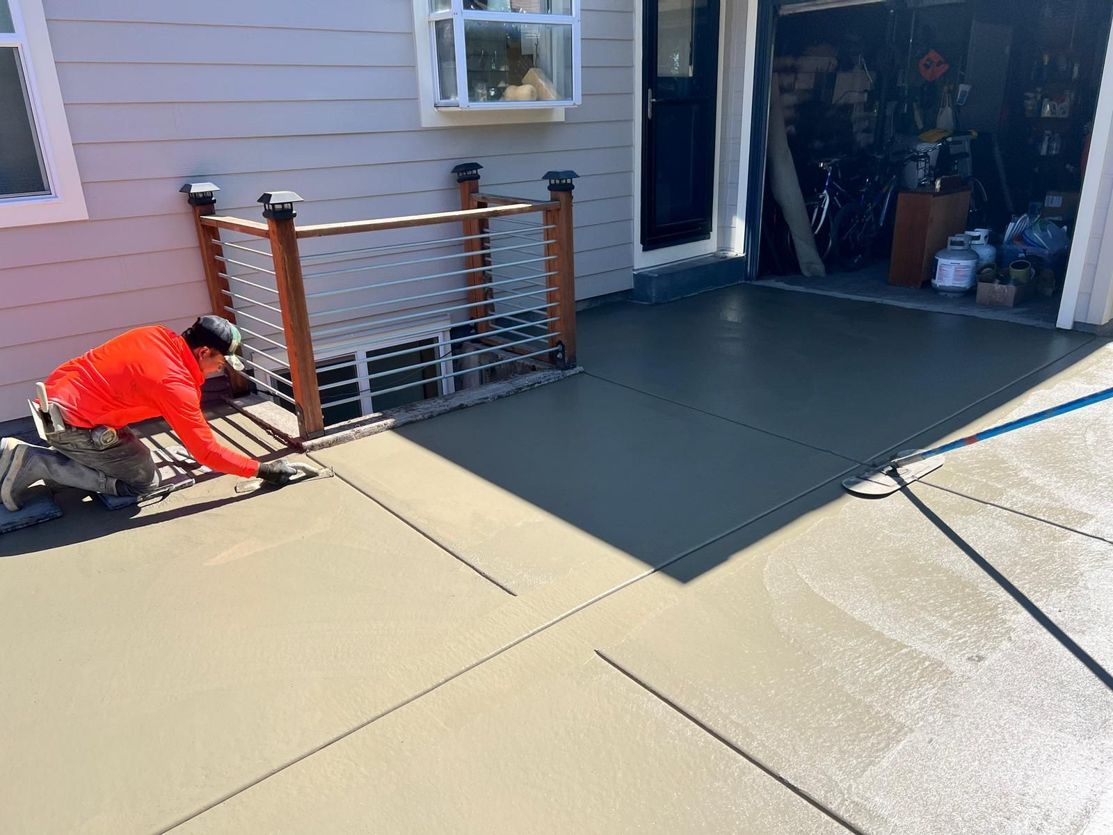 Man smoothing wet concrete patio with building and garage in background.