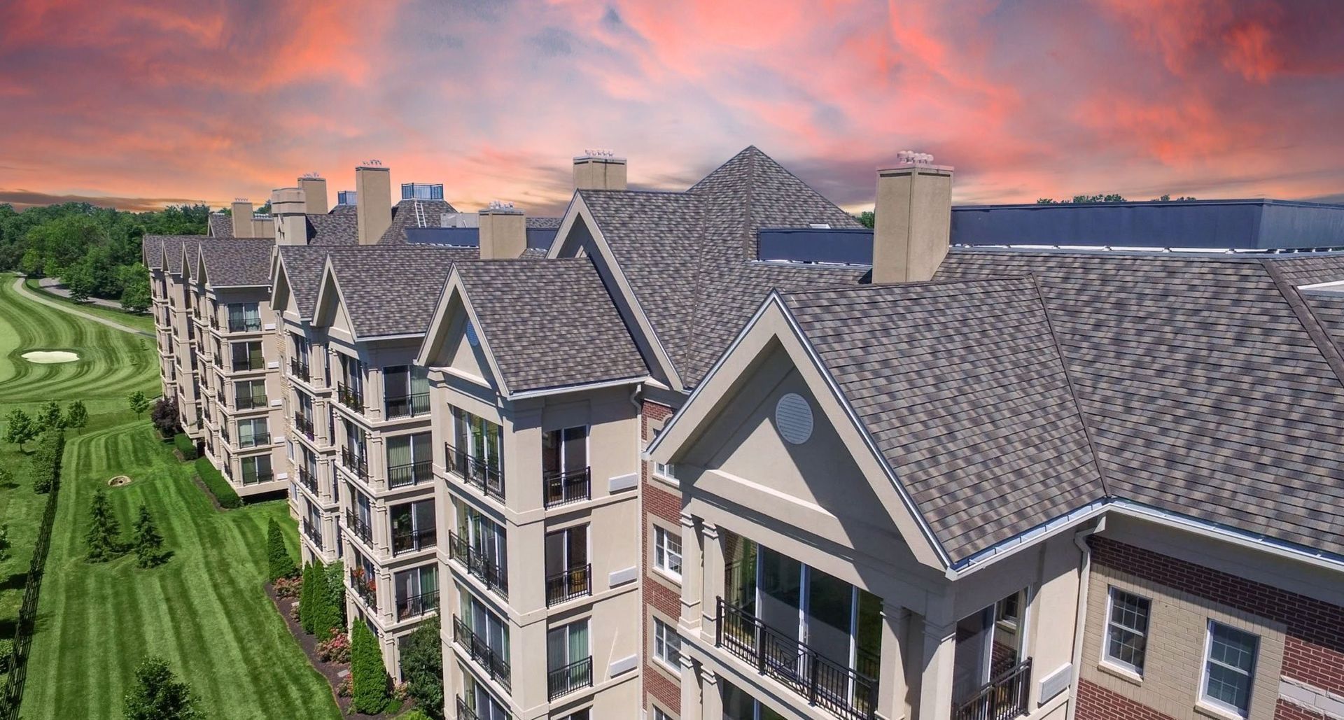 Aerial view of a multi-story building with a golf course on the left and a colorful sunset in the background.