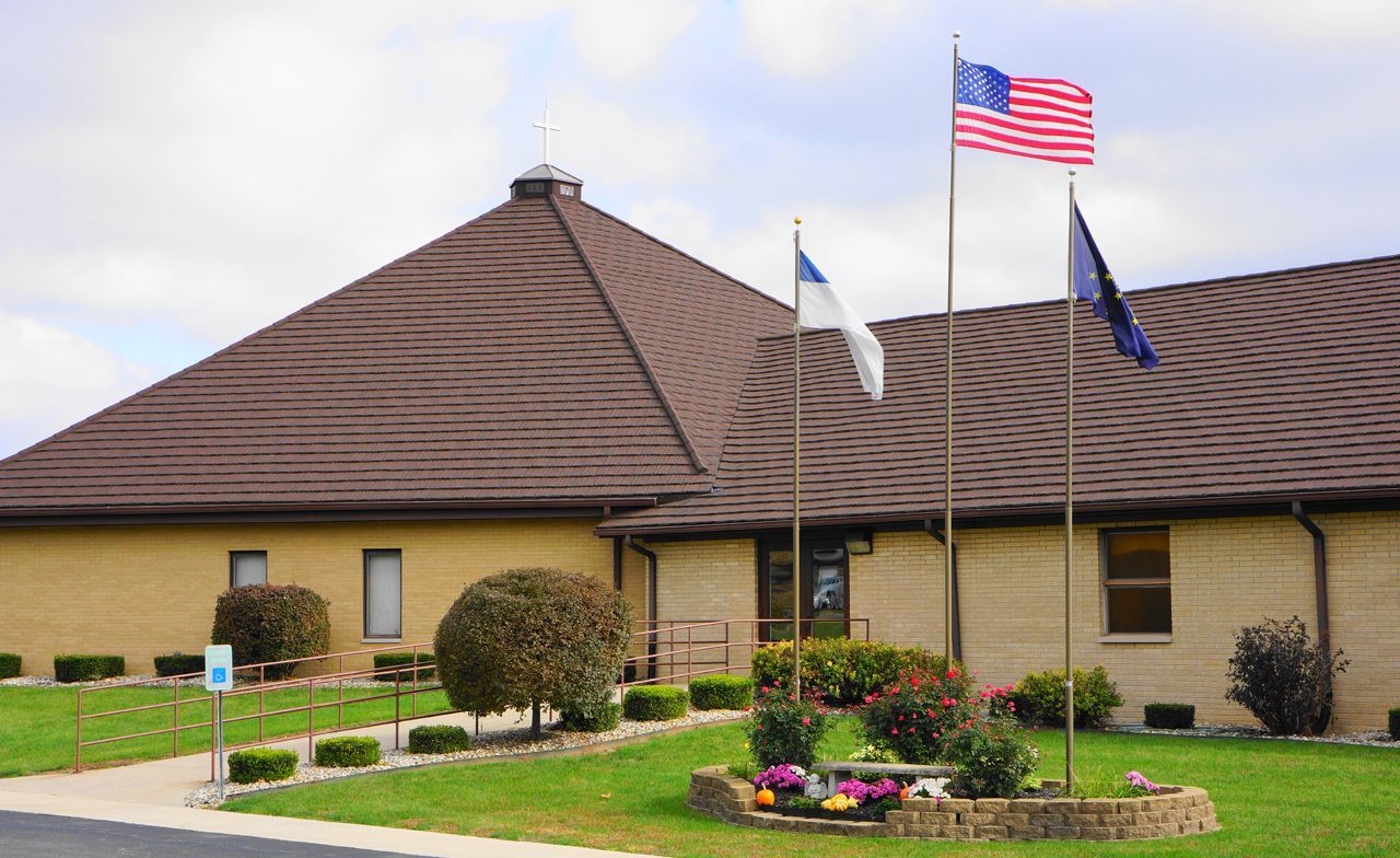 Exterior of a brick building with a brown roof; three flags fly in front: American, Christian, and another dark flag.