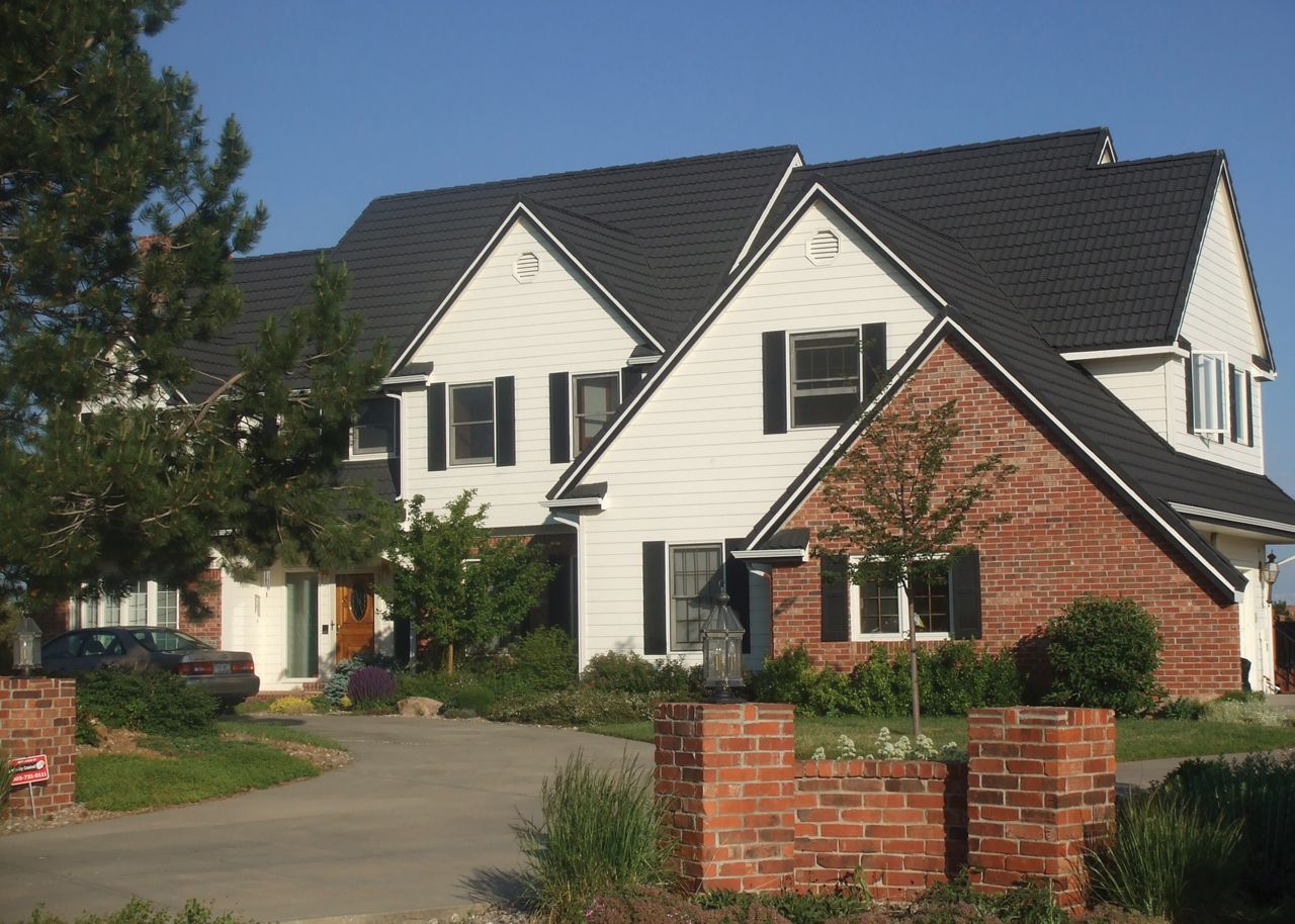 Two-story house with white siding, red brick accents, and a dark gray roof, with black shutters.