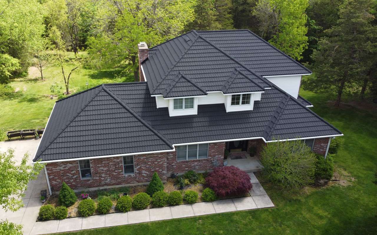 Aerial view of a house with a dark gray roof, brick and white exterior, and green lawn.