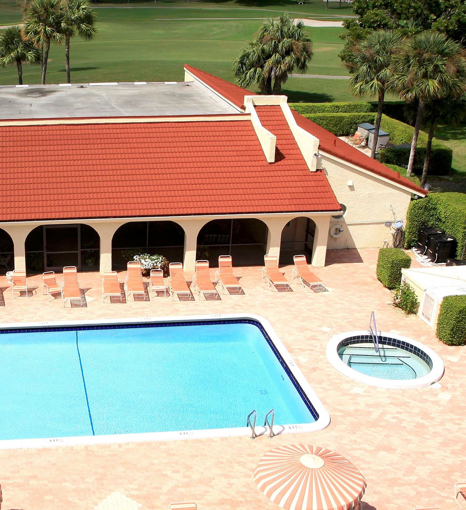 Swimming pool and spa next to a building with a red tile roof, surrounded by lounge chairs and greenery.