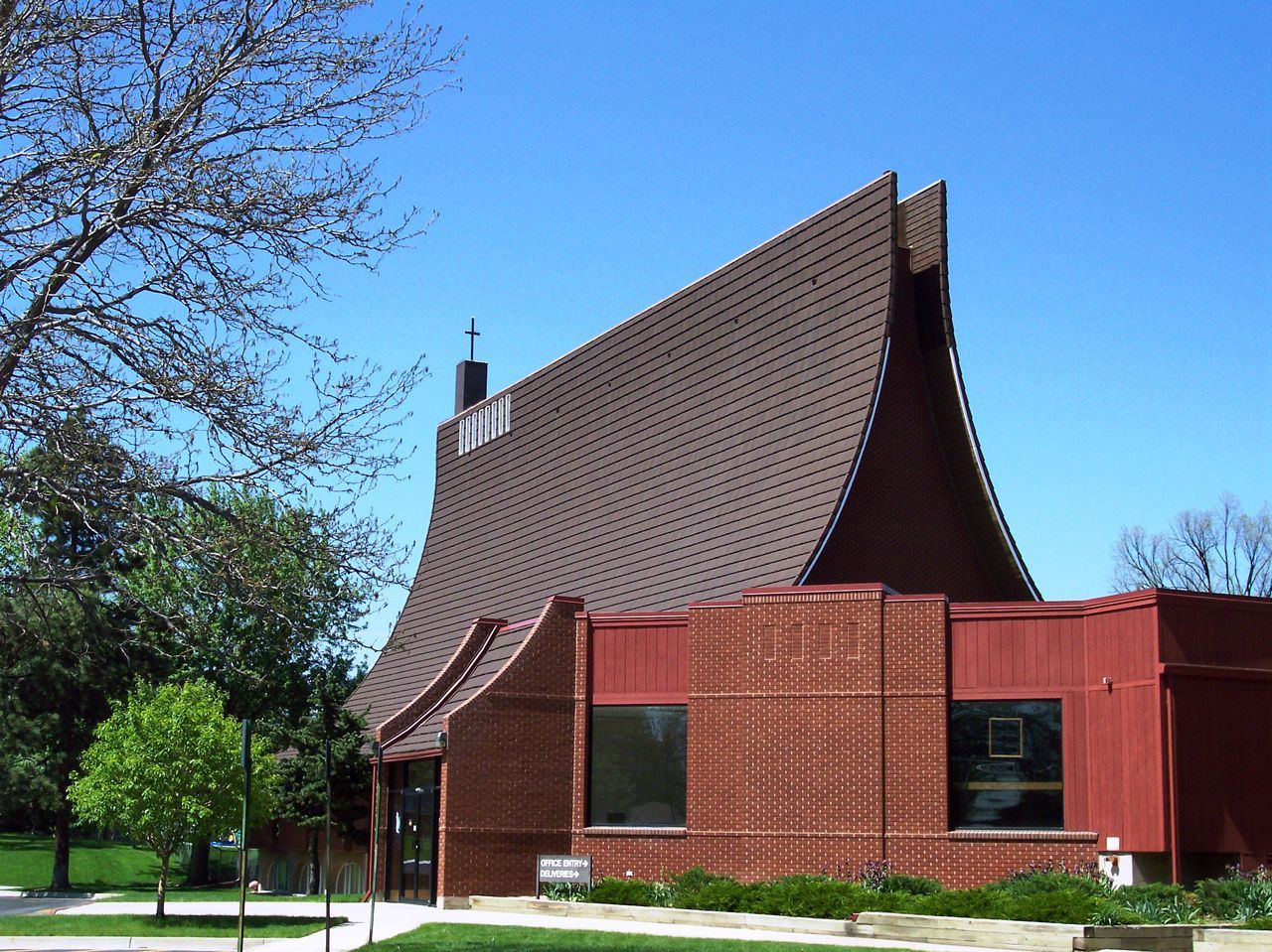 A modern church with a curved, brown-tiled roof and red brick facade against a blue sky.