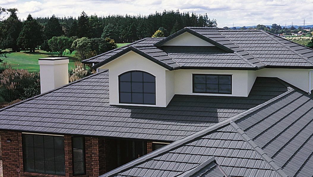House with dark gray metal roofing, a brick lower section, and a green lawn in the background.