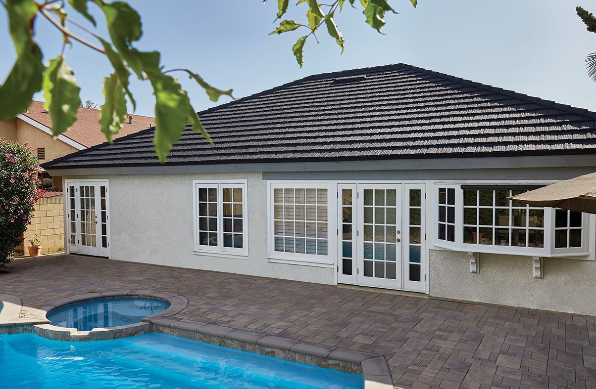 A light-colored building with white-framed doors and windows facing a pool. The roof is dark and made of shingles.