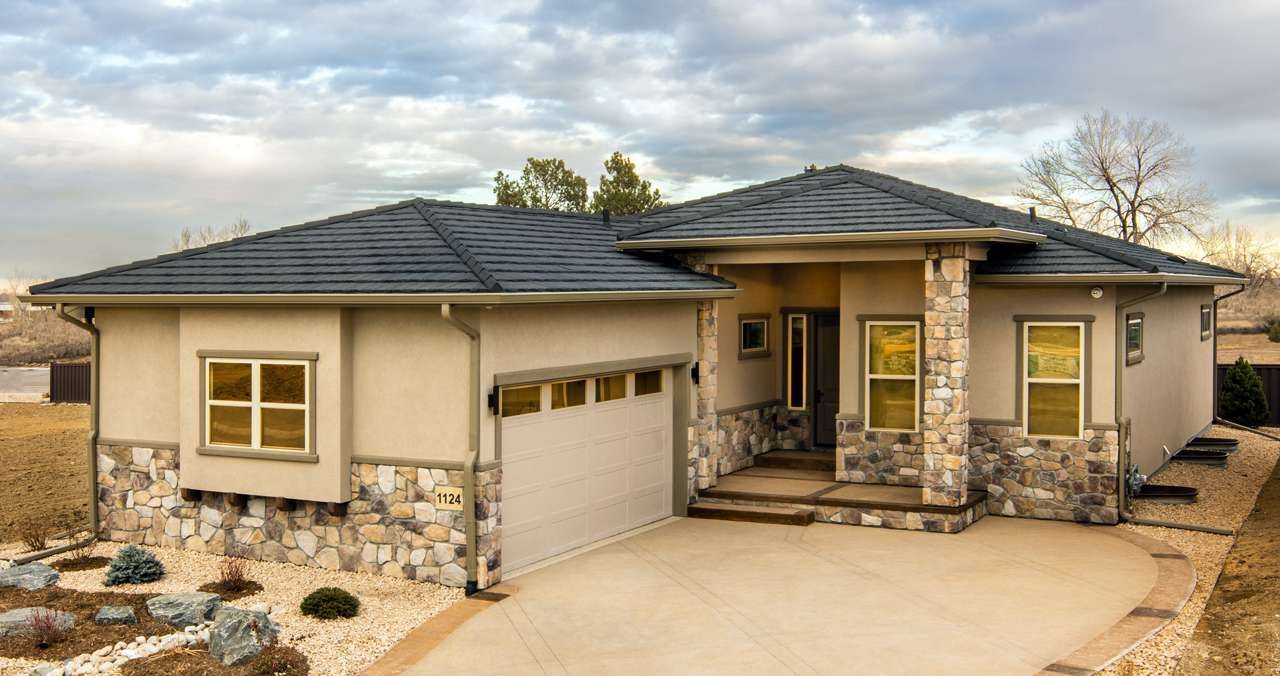 Beige house with stone accents, a dark roof, and a two-car garage, set against a cloudy sky.