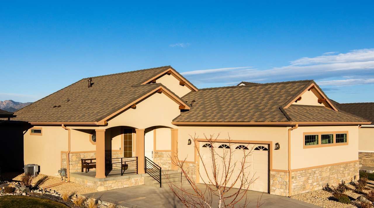 Tan stucco house with brown roof and garage under a blue sky. Features include stone accents and a covered porch.