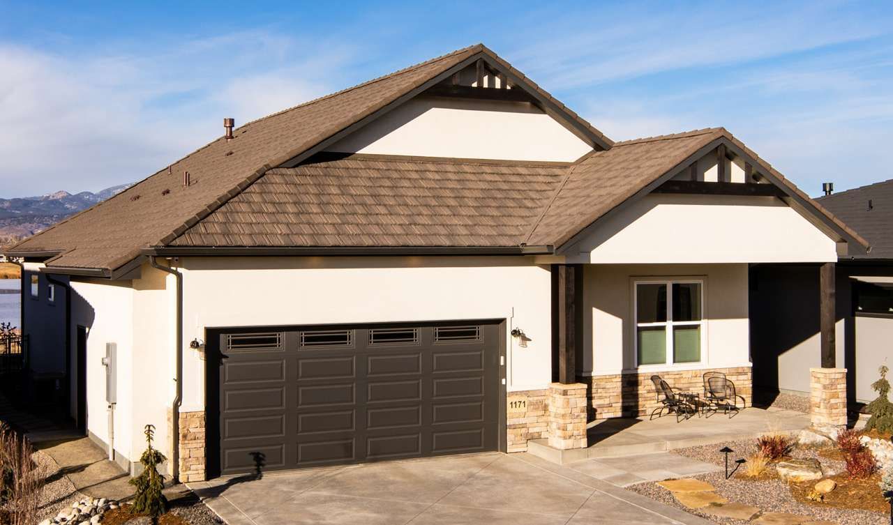 A modern house with a brown roof, tan stucco walls, and a dark gray garage door, set against a bright blue sky.