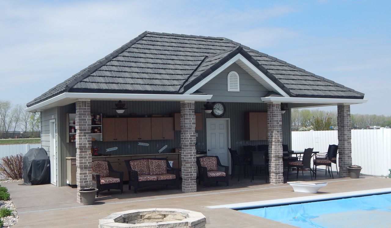 Poolside outdoor kitchen with gray roof, stone columns, and seating. Includes grill, cabinets, and fire pit.